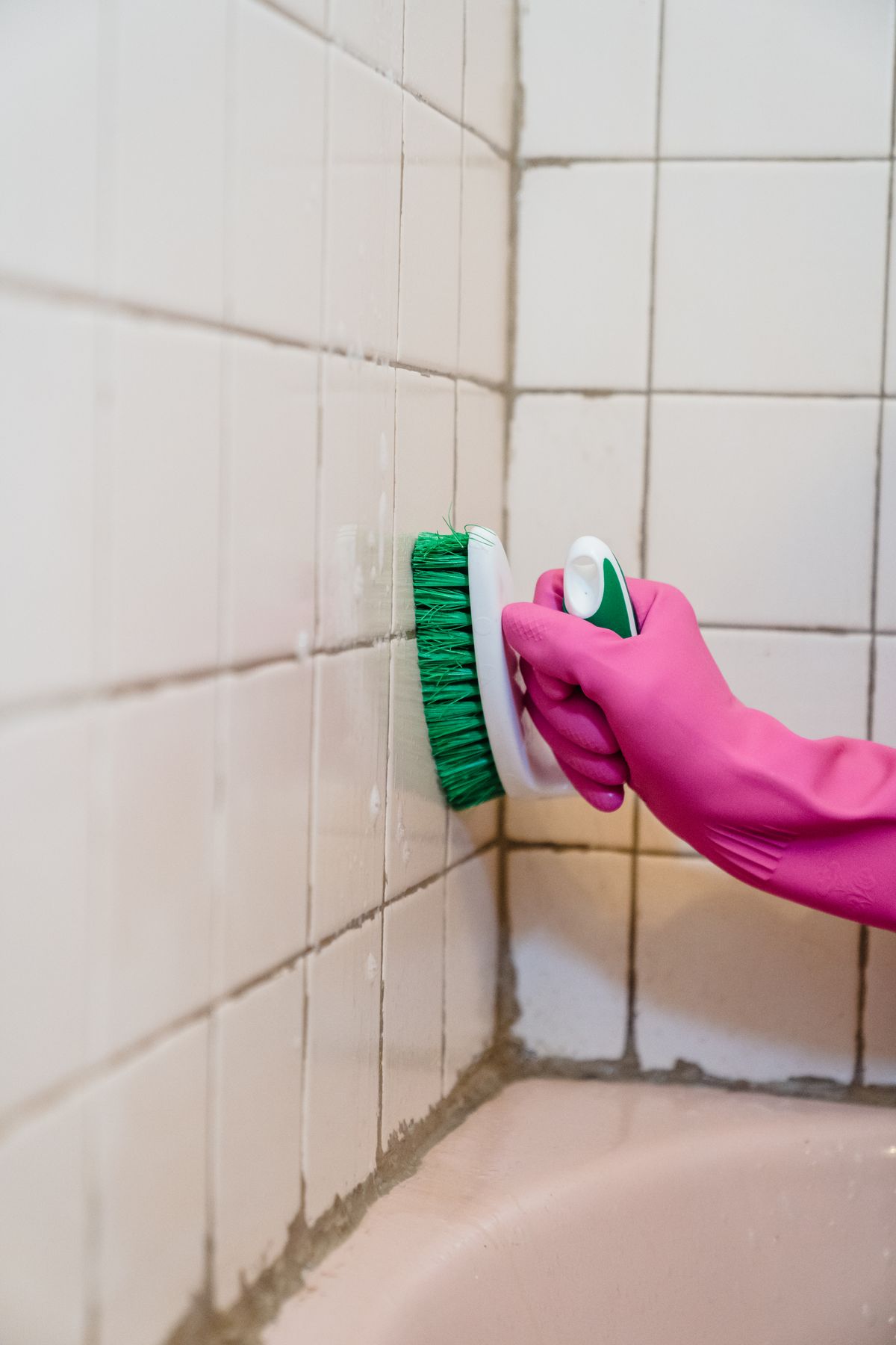 Cleaning bathroom tiles with a gloved hand